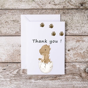 May include: A white thank you card with a brown dinosaur hatching from an egg. The card has brown dinosaur footprints in the top left corner and the text "Thank you!" in black.