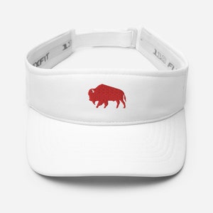Könnte beinhalten: Weißes Visier mit einem roten, gestickten Büffel-Logo. Das Visier hat einen gebogenen Schirm und einen verstellbaren Riemen. Die Marke Flexfit ist auf der Innenseite des Visiers sichtbar.