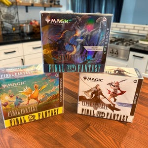 Op de afbeelding: Drie Magic the Gathering Final Fantasy kaartspeldozen. De bovenste doos is een Gift Bundle met duistere fantasy-kunst. Linksonder is een Chocobo Bundle met kleurrijke vogelillustraties. Rechtsonder is een Bundle met twee karakterfiguren.