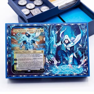 May include: A blue storage box for trading cards featuring a Jace, Multiverse Architect card illustration on the lid. The box lid displays a hooded figure in a white and blue outfit kneeling within a glowing blue magical circle.