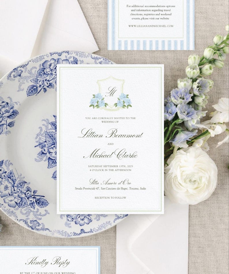 Op de afbeelding: Trouwkaart met een bloemenwapen en de namen Lillian Beaumont en Michael Clarke. De uitnodiging wordt omringd door een blauw-wit bloemenbord, bloemen en extra briefpapier. De tekst bevat de trouwdatum en -locatie.