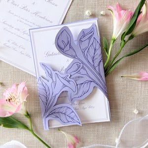 Peut inclure: Ensemble de faire-part de mariage avec un motif floral découpé au laser lavande. L'invitation comprend les noms Gabriella Ellen Rosen et Oliver Peter Henderson. Des fleurs roses et un ruban blanc ornent la papeterie sur un fond en lin neutre.