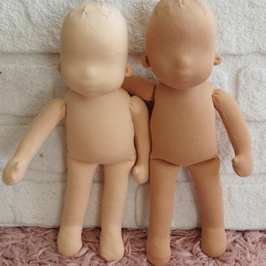 Puede incluir: Dos muñecas de tela beige en blanco con detalles cosidos. Las muñecas tienen una forma simple y redondeada con brazos y piernas. Las cabezas son de forma ovalada sin detalles faciales, listas para personalizar. Las muñecas están hechas de una tela suave y clara.