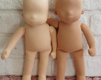 May include: Two blank, beige fabric dolls with stitched features. The dolls have a simple, rounded shape with arms and legs. The heads are oval-shaped with no facial details, ready for customization. The dolls are made of a soft, light-colored fabric.