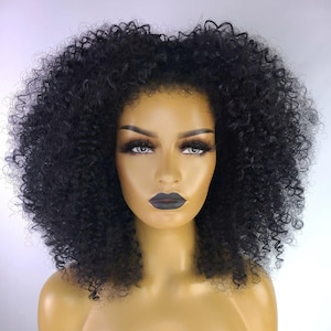 Peut inclure: Perruque bouclée noire avec une ligne de cheveux naturelle. La perruque est coiffée de boucles volumineuses et serrées. La tête de mannequin est entièrement maquillée, avec du rouge à lèvres foncé et de longs cils. Le fond est blanc uni.