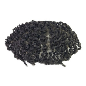 Pu&ograve; includere: Un'extension per capelli ricci neri, probabilmente una parrucca o un'estensione per capelli, su sfondo bianco. I capelli sono fittamente arricciati, con un aspetto naturale. L'extension &egrave; progettata per essere indossata sulla testa.