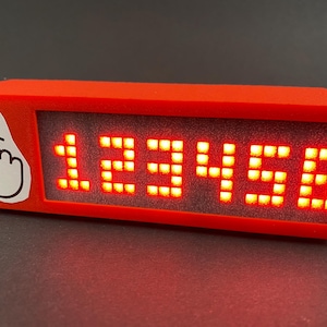 May include: A red rectangular box with a white hand pointing up and a red LED display showing the number 123456.