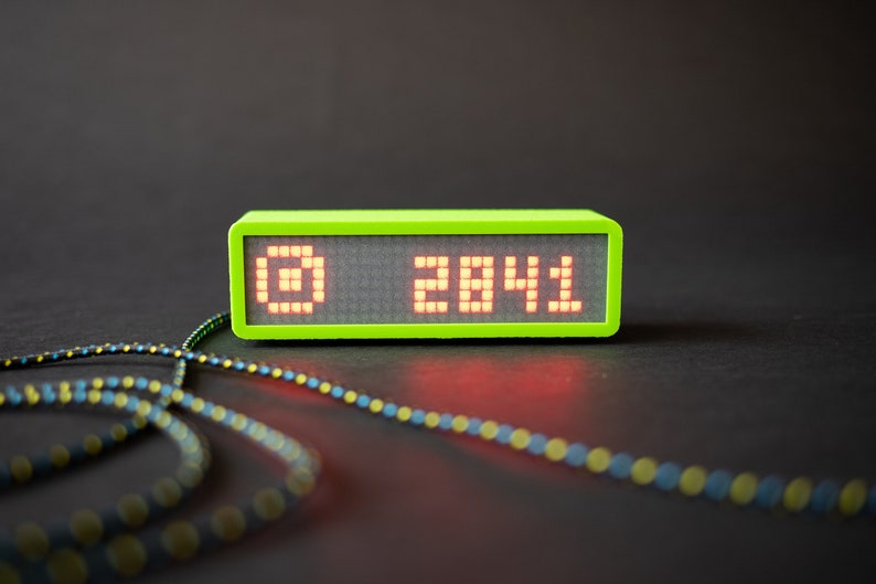 May include: A lime green digital clock with a red LED display showing the number 2041. The clock is sitting on a black surface with a black and yellow cord in front of it.