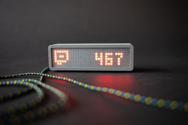 Puede incluir: Un dispositivo rectangular gris con una pantalla LED roja que muestra el n&uacute;mero "467" y un s&iacute;mbolo que parece un cuadrado con una l&iacute;nea diagonal.