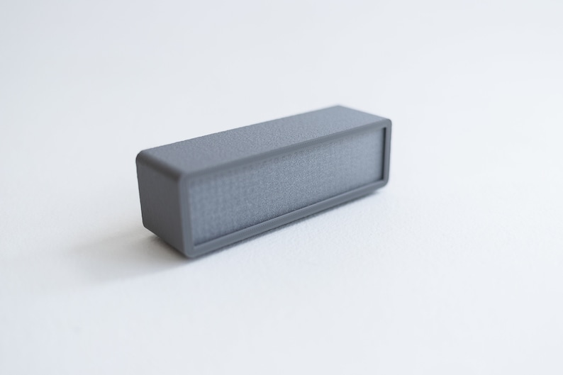 Puede incluir: Un peque&ntilde;o altavoz rectangular gris con una superficie texturizada.