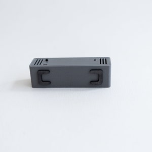 Puede incluir: Una caja rectangular gris con dos pies de goma negra en la parte inferior.