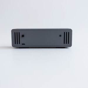 Puede incluir: Un dispositivo rectangular gris con dos juegos de peque&ntilde;as ventilaciones rectangulares a cada lado.