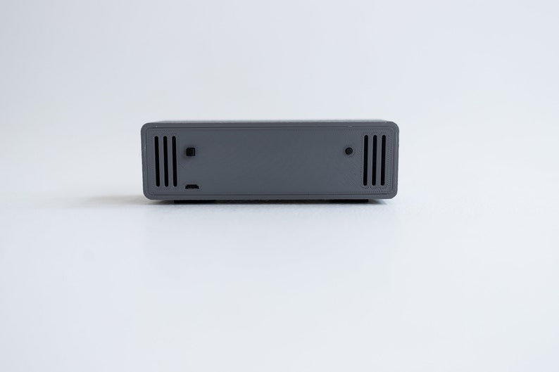Puede incluir: Un dispositivo rectangular gris con dos juegos de peque&ntilde;as ventilaciones rectangulares a cada lado.