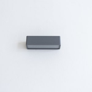 Puede incluir: Un aplique de luz rectangular gris con una superficie lisa.