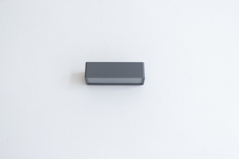 Puede incluir: Un aplique de luz rectangular gris con una superficie lisa.