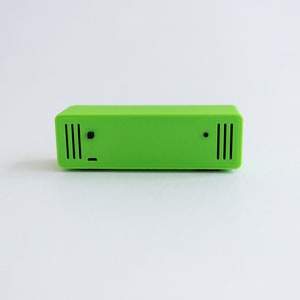 May include: A bright green rectangular device with a small black dot and two rows of vertical black lines on the front.