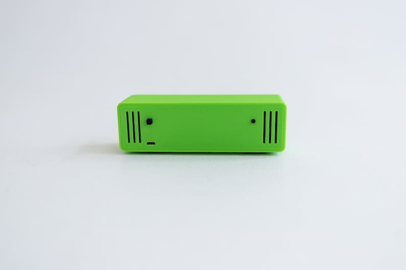 May include: A bright green rectangular device with a small black dot and two rows of vertical black lines on the front.