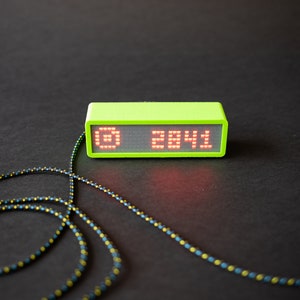May include: A lime green digital clock with a red LED display showing the time 28:41. The clock is connected to a black and yellow cord.