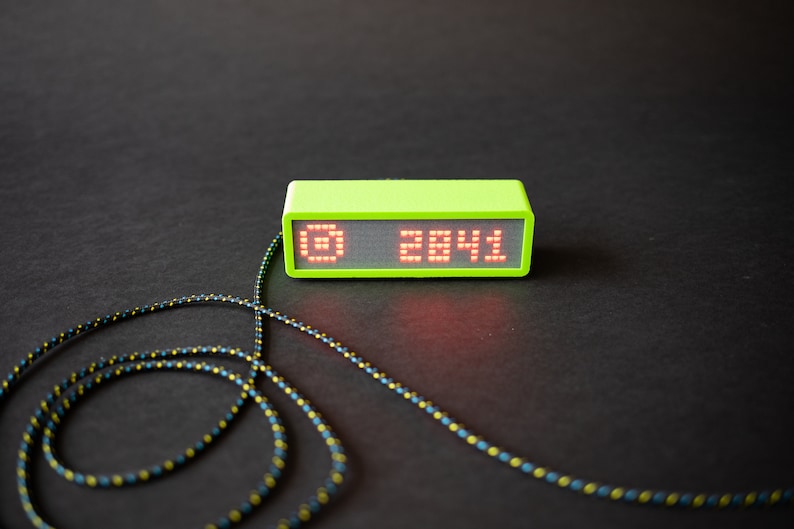 May include: A lime green digital clock with a red LED display showing the time 28:41. The clock is connected to a black and yellow cord.