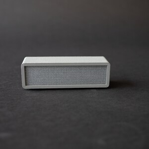 Puede incluir: Un peque&ntilde;o altavoz rectangular gris con una rejilla de tela.