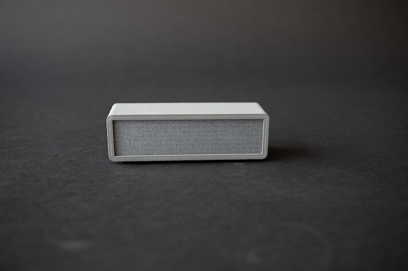Puede incluir: Un peque&ntilde;o altavoz rectangular gris con una rejilla de tela.