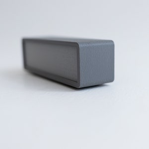 Puede incluir: Un altavoz rectangular gris con un acabado texturizado.