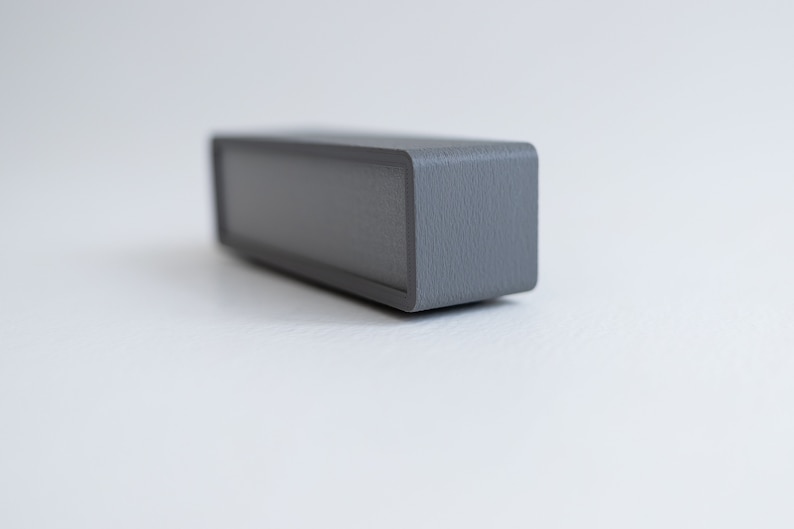 Puede incluir: Un altavoz rectangular gris con un acabado texturizado.