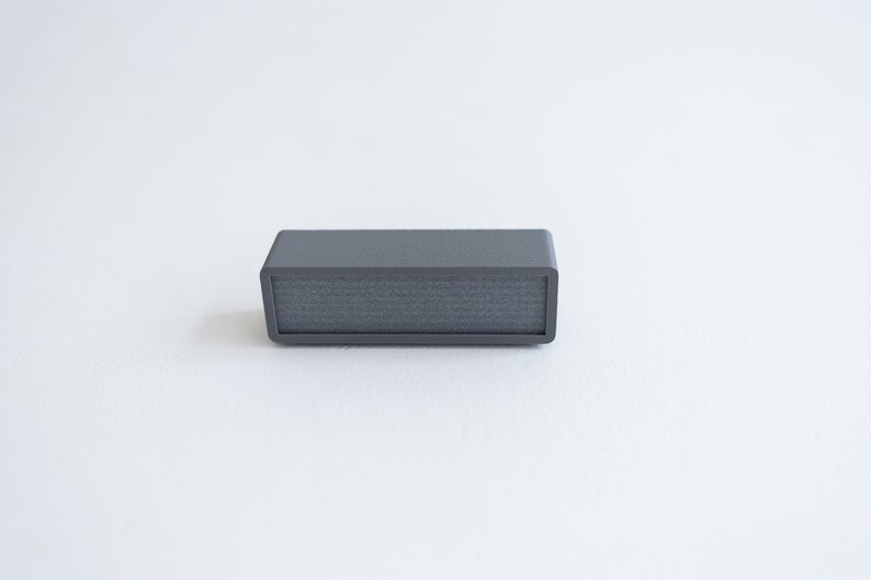 Puede incluir: Un peque&ntilde;o altavoz rectangular gris con una rejilla de tela.
