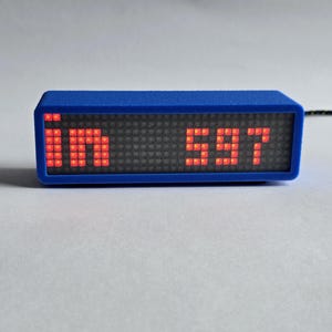 May include: A blue rectangular digital display showing the letters "in" and the number "597" in red. The display has a grid of small black squares. A black cable extends from the device.