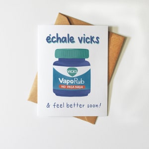 Könnte beinhalten: Eine weiße Karte mit einer blauen und grünen Illustration eines Vicks VapoRub-Glases. Die Karte sagt "échale vicks & feel better soon!" in schwarzem Text.