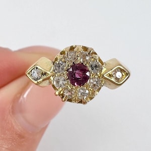 Könnte beinhalten: Ein goldener Ring mit einem runden Mittelstück, das von kleineren Steinen umgeben ist. Der mittlere Stein ist tiefrosa.