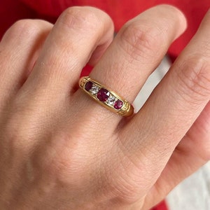 Könnte beinhalten: Ein Goldring mit fünf roten Edelsteinen und kleineren weißen Edelsteinen, die in die Band gefasst sind.