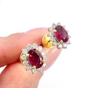 以下が含まれることがあります： ルビーとダイヤモンドのイヤリングのペア。イヤリングはゴールドでセットされており、ダイヤモンドのハローで囲まれたラウンドルビーが特徴です。
