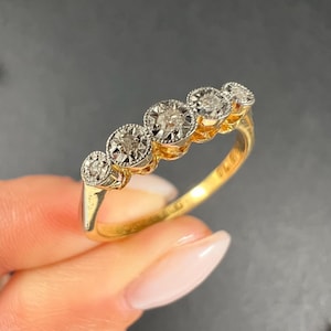 May include: A gold band ring with five round diamonds set in a row. The diamonds are bezel set and have a slightly raised profile.