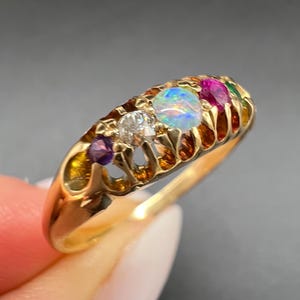 Peut inclure: Une bague en or ornée d'opale, de diamant, de rubis et d'améthyste. La bague présente un design complexe avec des détails ajourés. Les pierres précieuses sont disposées en rangée sur le dessus.