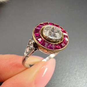 May include: A silver ring with a large round diamond surrounded by a halo of red rubies. The ring has a gold band.