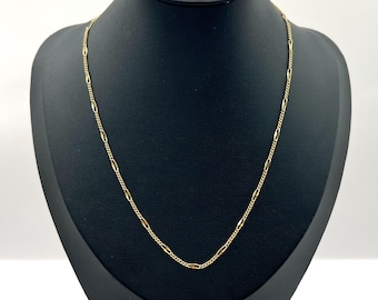 May include: A gold-colored necklace with a delicate chain design. The necklace is displayed on a black jewelry bust with a wooden base. The chain features a repeating pattern of small oval and bar-shaped links.