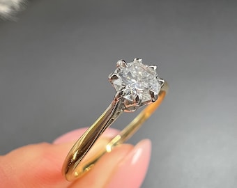May include: A gold and silver ring with a large, clear gemstone. The ring has a classic design with a gold band and a silver setting for the gemstone. The gemstone is round and faceted, catching the light.