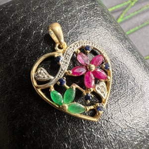 May include: A gold heart-shaped pendant with a floral design. The pendant features red, green, and blue gemstones.