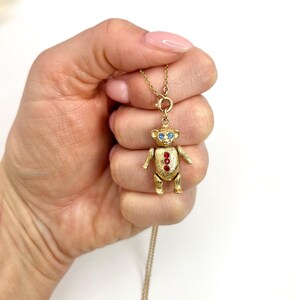 Op de afbeelding: Een gouden ketting met een teddybeerbedel. De beer heeft blauwe ogen en rode edelsteenaccenten.
