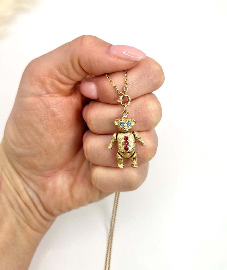 Op de afbeelding: Een gouden ketting met een teddybeerbedel. De beer heeft blauwe ogen en rode edelsteenaccenten.