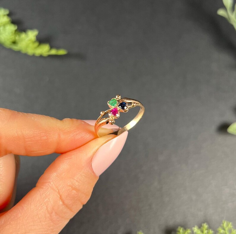 May include: A gold ring with three small gemstones: a green emerald, a red ruby, and a blue sapphire. The ring is set in a delicate, twisted band.