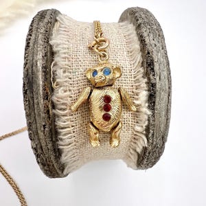 Op de afbeelding: Een gouden ketting met een teddybeerbedel. De beer heeft blauwe ogen en rode strass steentjes.