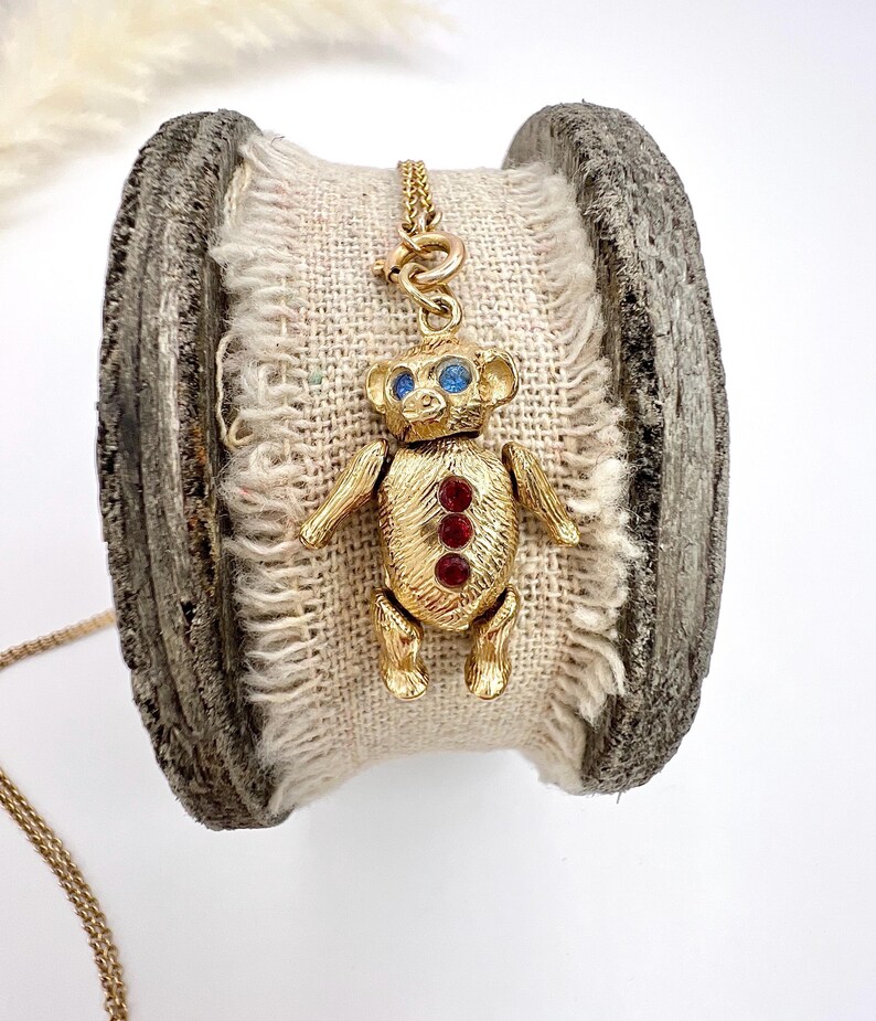 Op de afbeelding: Een gouden ketting met een teddybeerbedel. De beer heeft blauwe ogen en rode strass steentjes.