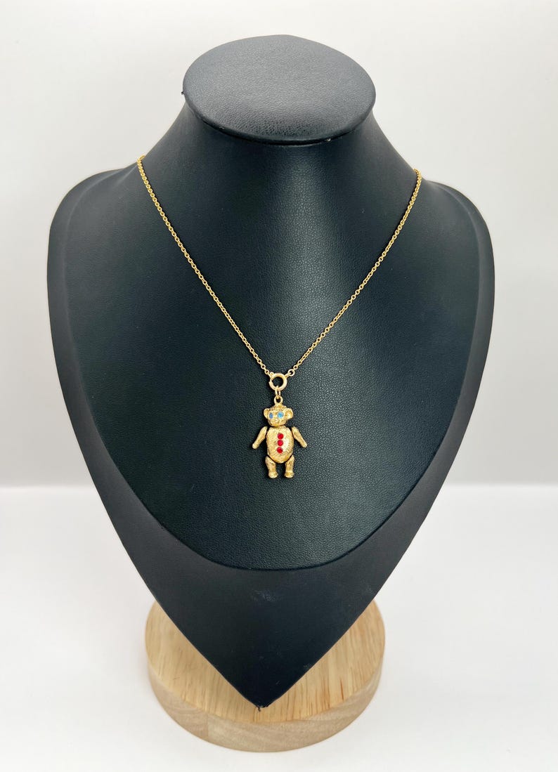Op de afbeelding: Een gouden ketting met een teddybeer hanger. De beer heeft rode en blauwe emaille accenten.