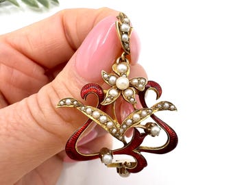 Könnte beinhalten: Vintage goldfarbener Anhänger mit floralem Design, einer zentralen Blüte und geschwungenen roten Emaille-Akzenten. Der Anhänger ist mit kleinen, runden Perlen verziert. Das Design ist aufwendig und detailliert und zeigt eine klassische Ästhetik.