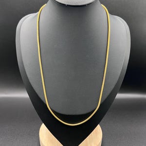 Op de afbeelding: Een goudkleurige ketting met een fijn, uniform en getextureerd schakelontwerp. De ketting is cirkelvormig en vertoont over de gehele lengte een consistente metallic gele afwerking, die gelijkmatig op de displayvorm rust.