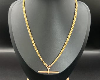 Könnte beinhalten: Eine goldene Kettenkette mit einem T-Bar-Verschluss. Die Kette befindet sich auf einem schwarzen Präsentationsständer.