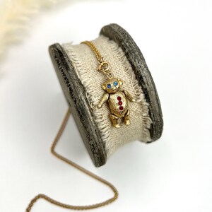 Op de afbeelding: Een gouden ketting met een teddybeerbedel. De beer heeft rode en blauwe edelsteenaccenten.