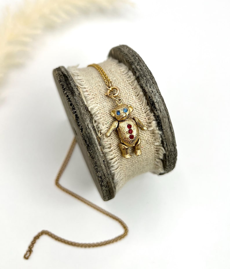 Op de afbeelding: Een gouden ketting met een teddybeerbedel. De beer heeft rode en blauwe edelsteenaccenten.